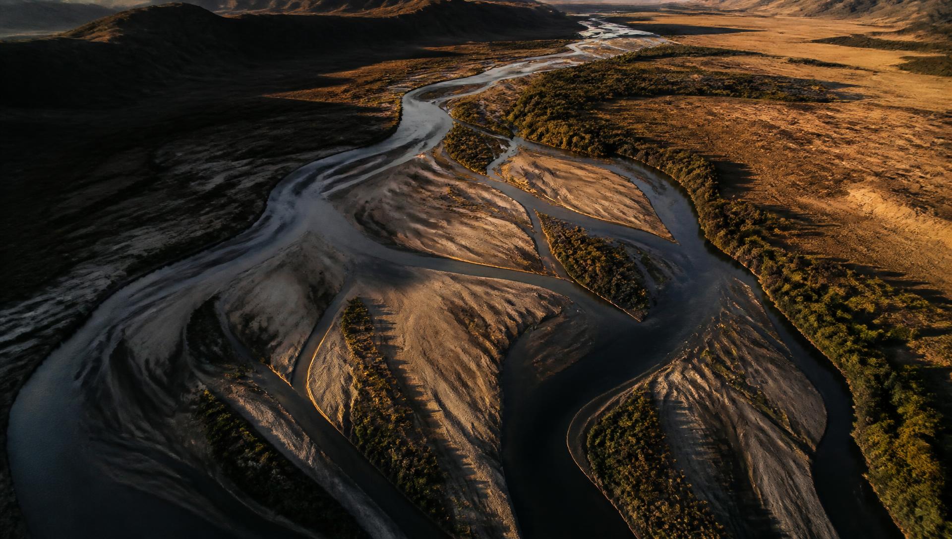 Aerial view of a braided river system and sandbars across arid plains at golden hour
